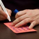 Stift in einer Hand, welche gerade auf eine Moderationskarte schreibt