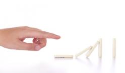 Hand zeigt auf Dominosteine, welche zur Hälfe umgefallen sind