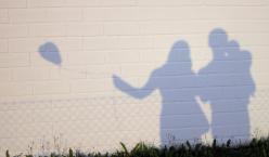 Schatten von Vater, Mutter und Kind mit einem Luftabllon an einer Mauer