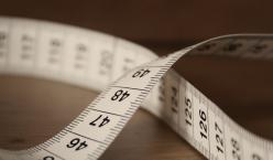 Ein Maßband liegt verschlungen auf einem Holztisch