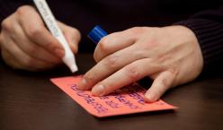 Stift in einer Hand, welche gerade auf eine Moderationskarte schreibt